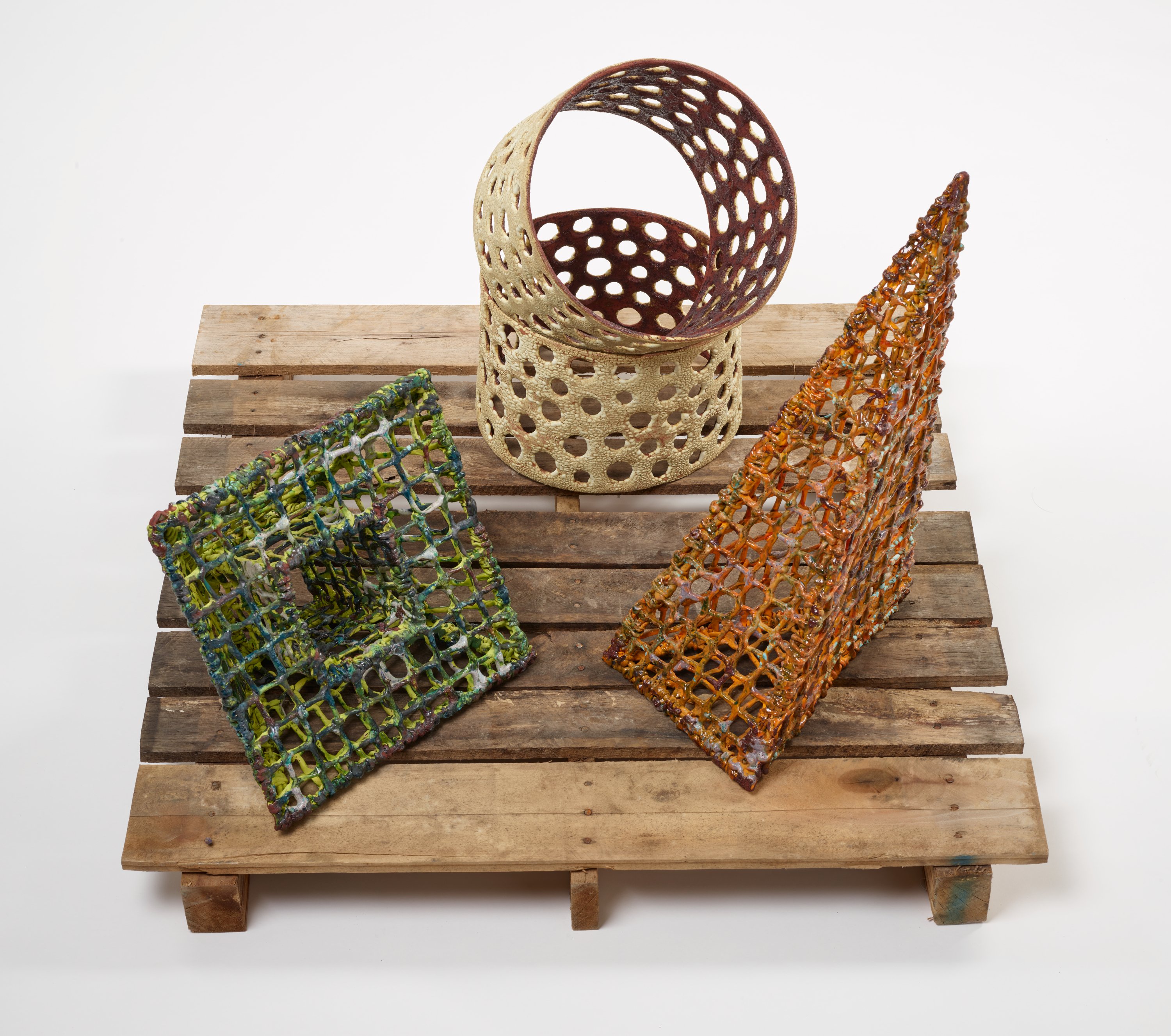 Three woven objects of different shapes rest on a wooden pallet.
