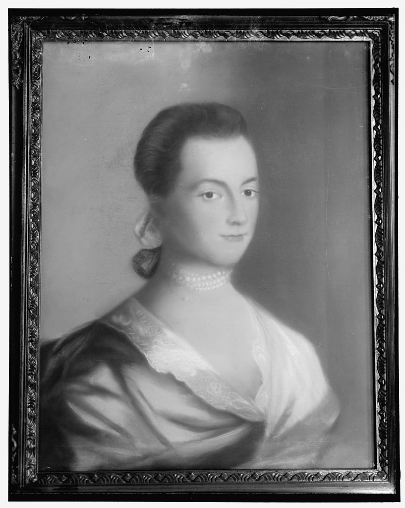 A black and white portrait of Abigail Adams with a slight smile, wearing a lace-trimmed dress and pearl necklace.