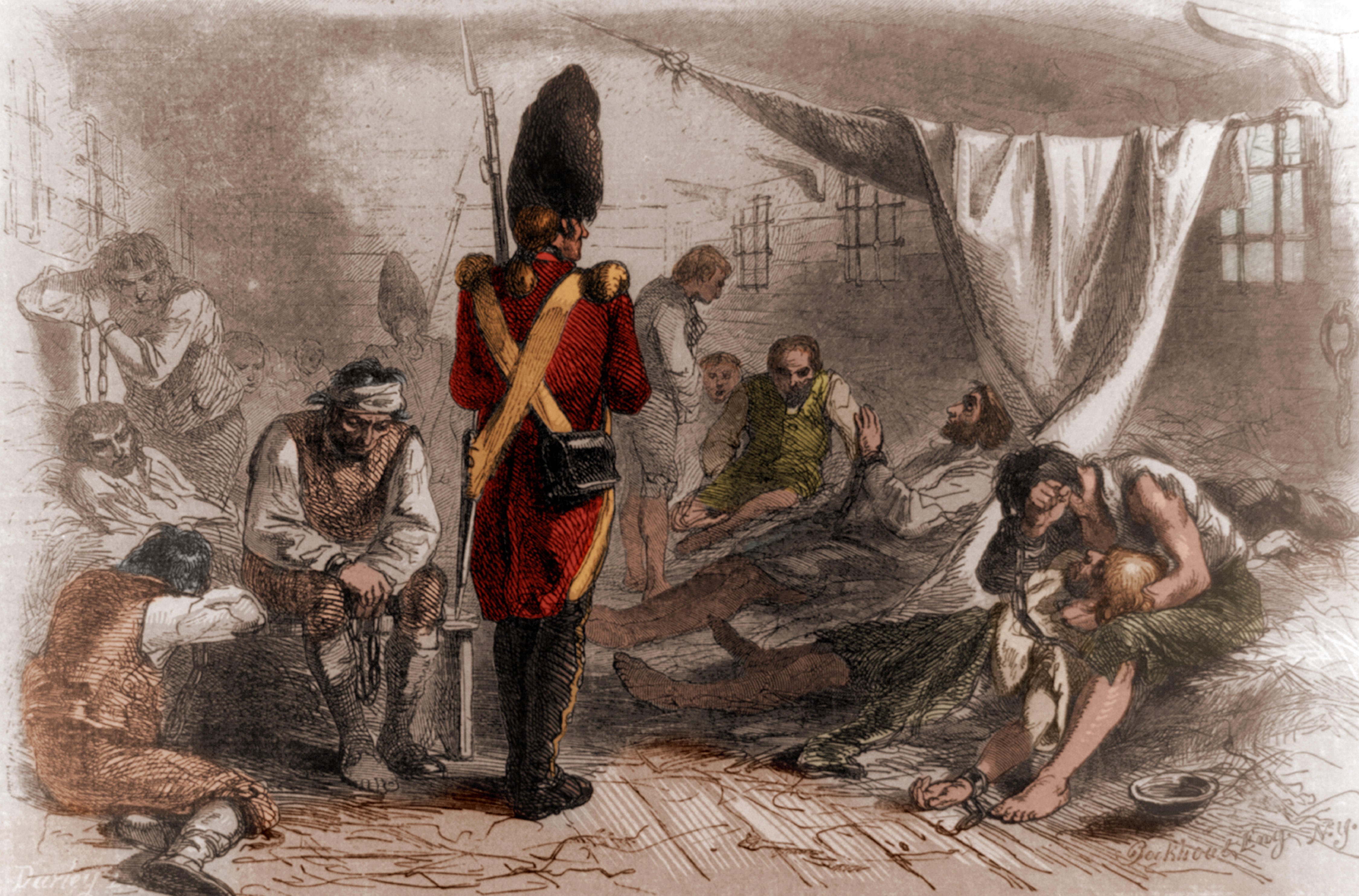 An image of a colored engraving shows a British soldier in his red uniform standing guard over several prisoners inside a cramped room. Some prisoners are chained and many are slumped over and appear unwell.