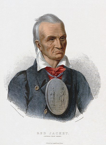 A colored portrait of an Indigenous man with white hair and a stern expression. He wears a colonial White man's clothing and a large medallion showing him in tribal clothing shaking hands with George Washington, dated 1792. Writing below the portrait read