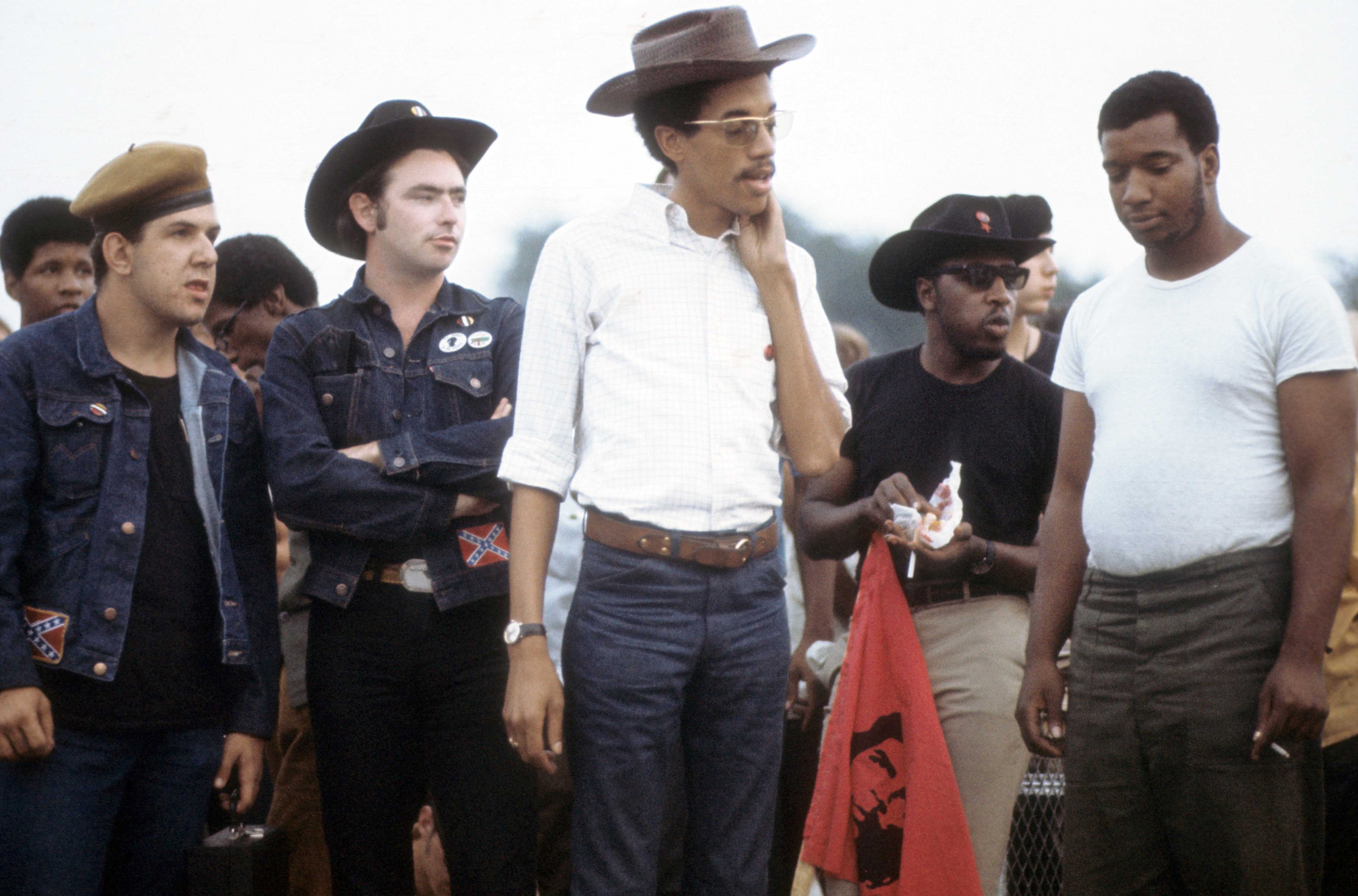 A colored photo shows two White Young Patriots members standing near to and observing three Black Panther Party leaders.